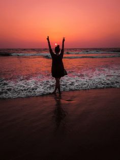 a woman standing on top of a beach next to the ocean with her arms in the air