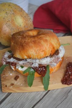 a sandwich with meat and cheese on a wooden cutting board next to bread buns