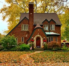 a large brick house surrounded by trees and leaves on the ground in front of it