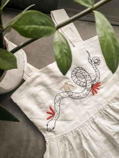 a white dress with a snake embroidered on the front and side, sitting next to a potted plant