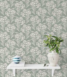 a white vase sitting on top of a table next to a wallpapered wall