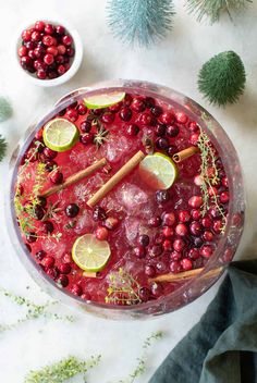 a drink in a glass with cranberries, limes and cinnamon sticks on the rim