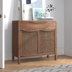 a wooden cabinet with wicker doors in a white room next to a door and rug