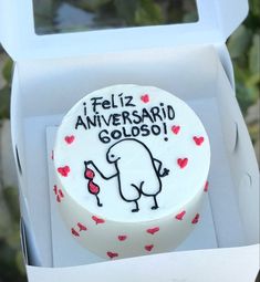 a white cake in a box with red hearts on the inside and writing i feliz aniversaro goloso