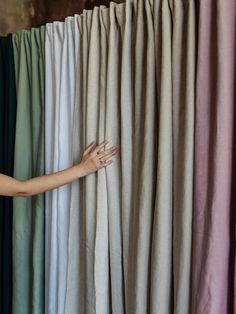 a woman's hand is on the curtain in front of several colored draperies