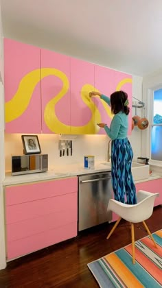 a woman is painting the wall in her kitchen with pink and yellow paint on it