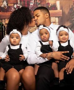 a man and woman sitting next to each other on a couch with two babies in front of them