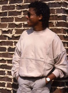 a young man standing in front of a brick wall with his hands in his pockets