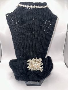 a black knitted sweater with pearls and beads on the collar is displayed in front of a pair of high heeled shoes