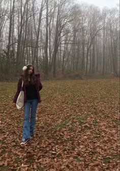 a woman standing in the middle of a leaf covered field