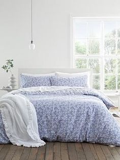 a bedroom with white walls and wooden floors has a blue floral comforter on the bed