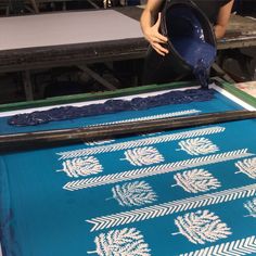 a woman is working on an art project with blue fabric and white leaves in the background