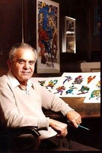 an older man sitting in front of a desk with pictures on the wall behind him