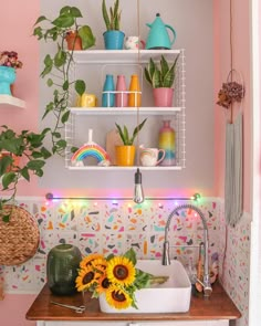 a kitchen sink with sunflowers and other decorations on the shelf above it in front of a pink wall