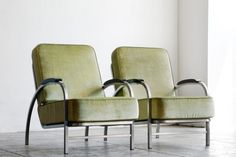 two green chairs sitting next to each other on top of a tile floor in front of a white wall