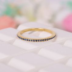 a yellow gold ring with blue sapphire stones on top of a white keyboard and flowers in the background