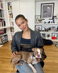 a woman holding two small dogs in her lap while sitting on the floor next to bookshelves