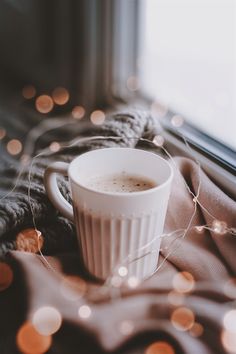 a cup of coffee sitting on top of a blanket next to a window sill