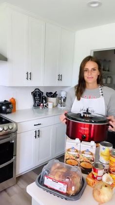 a woman standing in a kitchen holding an open crock pot with food on it