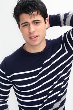 a young man with his hand on his head wearing a striped shirt and blue jeans