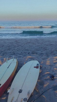 two surfboards are laying on the sand at the beach