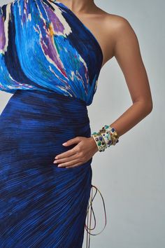 The mira dress is a one-shoulder dress that combines dual ikat-inspired and self-print fabrics. It features hand micro pleats, drawing inspiration from sari styles, and includes adjustable drawstrings for the sleeves and length, allowing for a personalized fit and elegant appeal. Blue Sun Dress, Puerto Galera, Drawstring Sleeve, Printed Silk Dress, Sari Dress, Blue Lily, Romper And Jacket, Silk Ikat, Indian Fabric