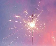 a close up of a sparkler on a purple and blue sky with clouds in the background