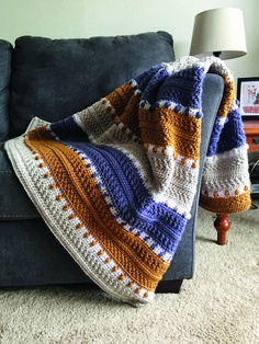 a crocheted blanket sitting on top of a gray couch next to a lamp