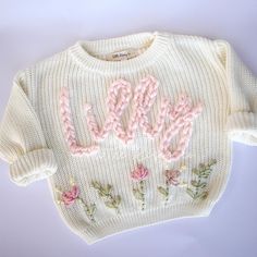 a knitted sweater with the word love spelled out in pink yarn and flowers on it