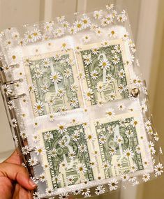 a person holding up a small album with dollar bills in the middle and daisies on it