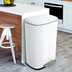 a kitchen with a white counter top next to a bar stool and an open trash can