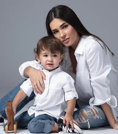 a woman sitting next to a child on the floor with her arms around her chest