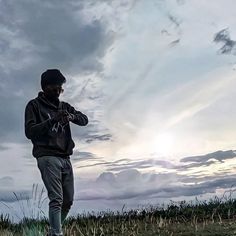 a man standing on top of a lush green field under a cloudy blue and white sky