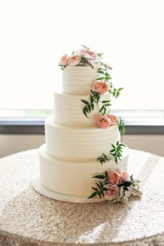 a white wedding cake with pink flowers on top and greenery on the bottom, sitting on a table