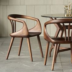 two wooden chairs sitting next to each other on top of a tile floor near a table