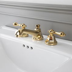 two golden faucets on the side of a white sink