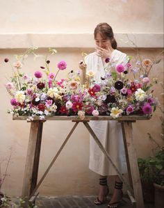 a woman standing in front of a wooden table with flowers on it and covering her face