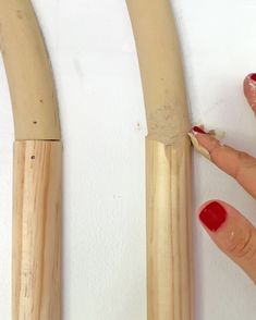 a hand holding a red nail next to two large wooden objects on a white wall