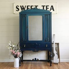 a blue cabinet sitting on top of a wooden floor next to a vase with flowers