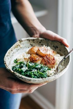 a person holding a bowl filled with rice and meat on top of spinach leaves