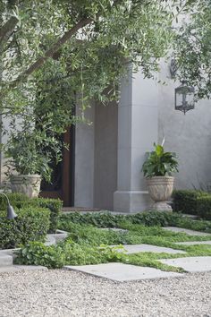 a man sitting on a bench in front of a building with trees and plants around it