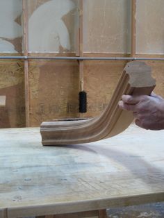 a person holding a piece of wood on top of a wooden table in a room