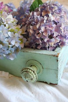 some purple flowers are in a wooden box on a white sheet with the color swatches