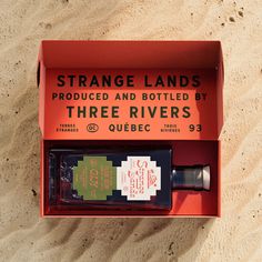 an orange box with two bottles in it sitting on the sand next to a bottle of liquor