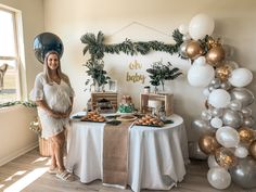 a pregnant woman standing in front of a table with balloons and desserts on it