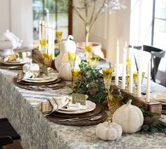 the table is set with white pumpkins, candles and greenery for thanksgiving dinner