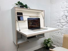 an open laptop computer sitting on top of a white desk next to a potted plant