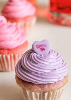 three cupcakes with pink frosting and hearts on top are sitting next to each other