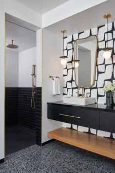 a modern bathroom with black and white tiles on the wall, gold trim around the sink