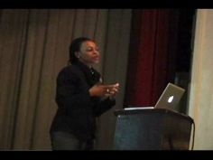 a woman standing in front of a podium with a laptop on her lap and talking